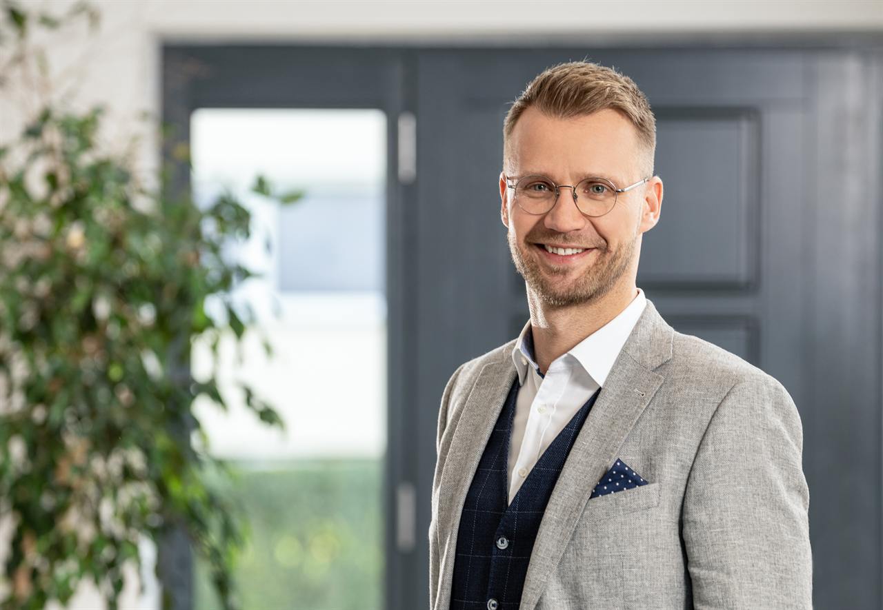 Thomas Hacker, Finanzierungsberater aus Itzehoe, steht lächelnd in einem hellen Eingangsbereich